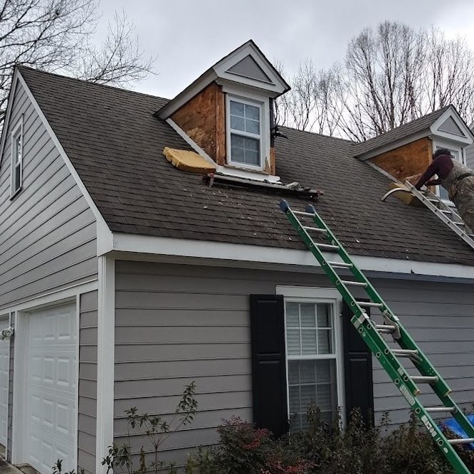 A ladder is poised to ascend a roof system where the roof is being prepped to be replaced.