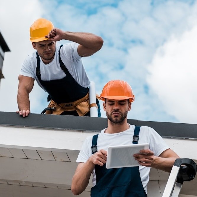 Two roofers are working on a roofing report for a metal roofing system.